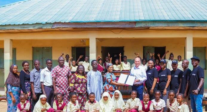 *ABUMET‘s general manager, Alexander  Hausner presenting a document donating chairs and desks to the Principal of Junior Secondary School, Aleyita, Mrs. Ngozi Charity Odeke, as teachers and students join in for a group photograph...Abuja, recently