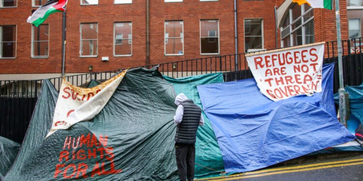 People stand by rows of tents, near the International Protection Office (IPO) in Dublin on April 30, 2024, which has become a tented village with migrants and asylum seekers sleeping on the footpaths and roads outside. Ireland's prime minister Simon Harris warned on Sunday that Dublin would take action to stem an influx of asylum seekers from Northern Ireland, the British territory across the border. (Photo by PAUL FAITH / AFP) (Photo by PAUL FAITH/AFP via Getty Images)